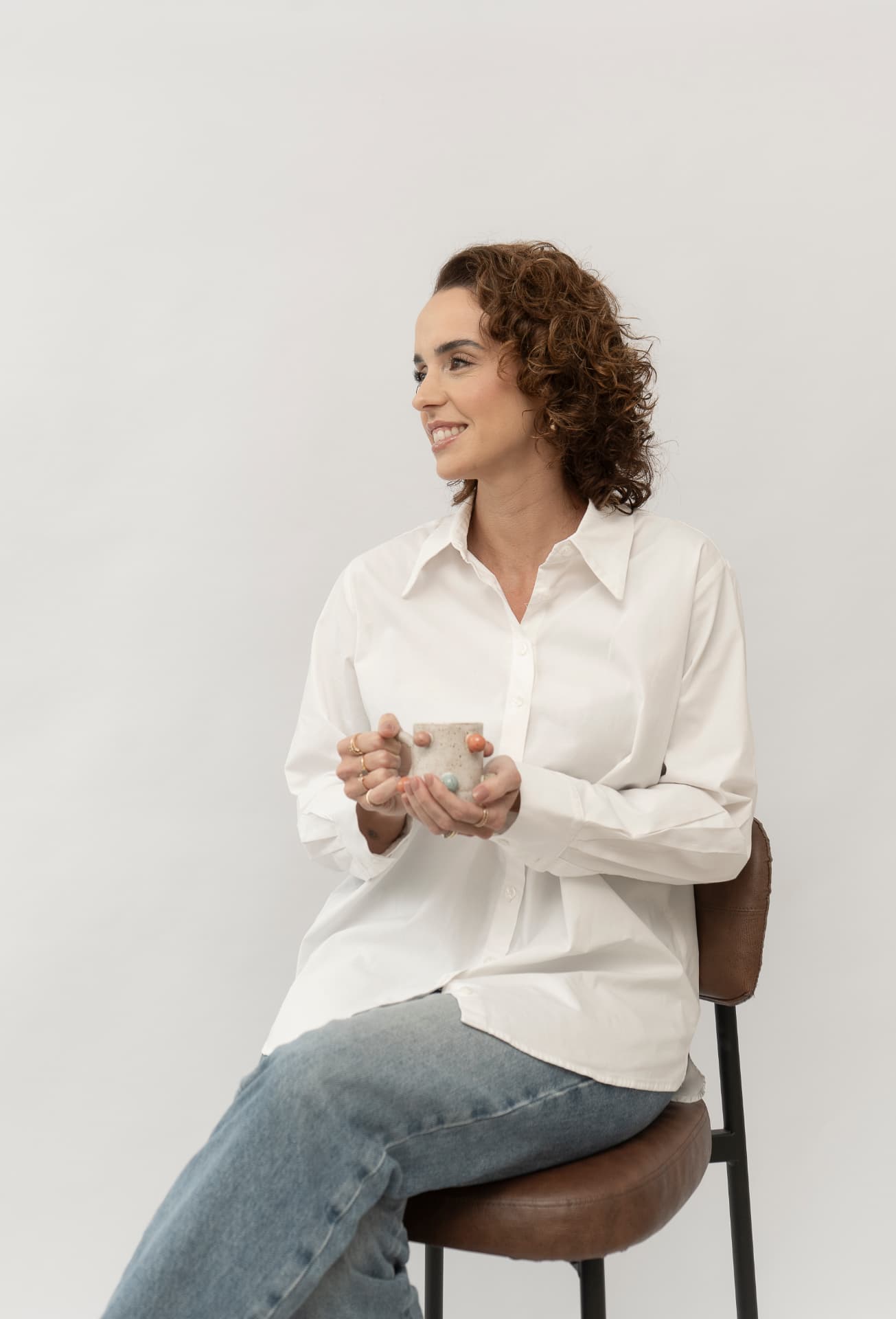 Camilla Veronezi, psicóloga, sentada sorrindo com uma caneca nas mãos
